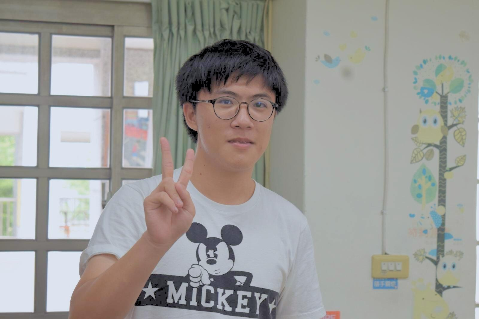 Portrait of Martin Chen standing indoors and making a peace sign.